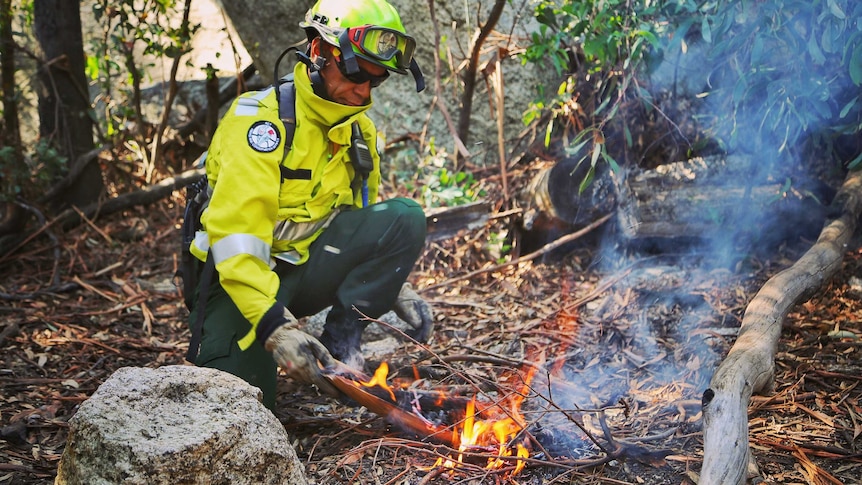 A man in fear gear places burning bark on the ground.