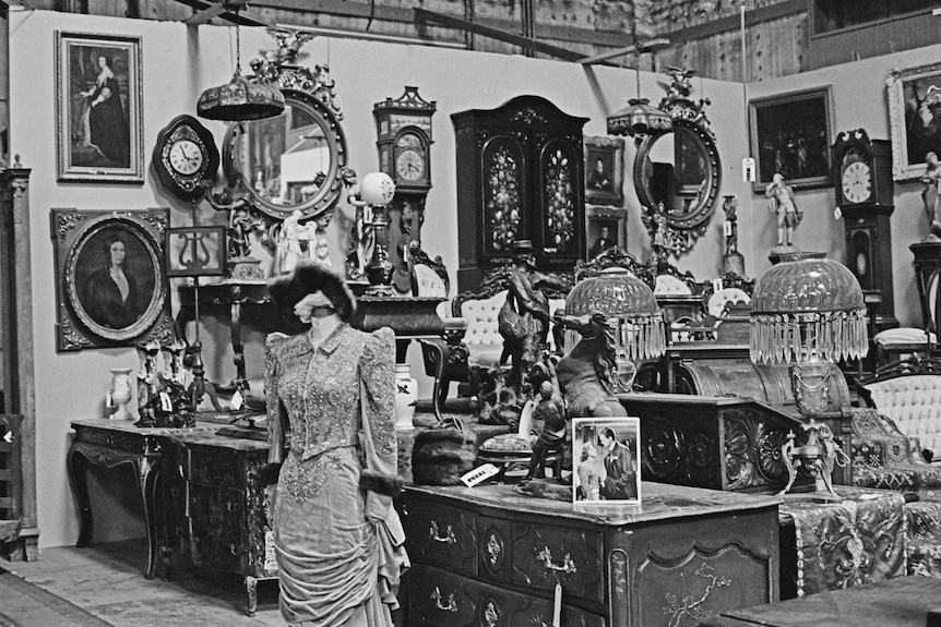 a black and white image with costumes, furniture, clocks and paintings. 