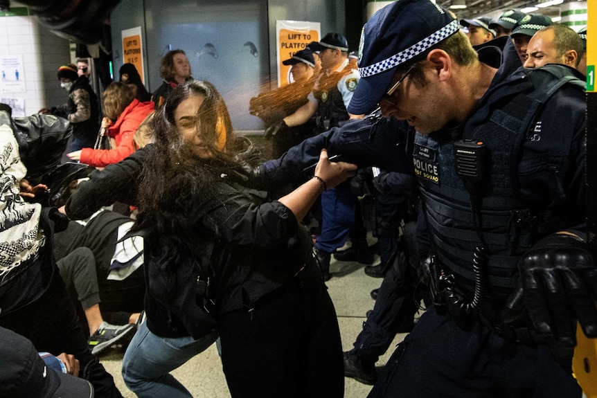 police stand infront of protesters as they spray pepper spray at a woman's face in Central Station