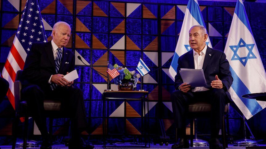 US President Joe Biden sits next to Israeli Prime Minister Benjamin Netanyahu on stage in front of their countrys' flags. 