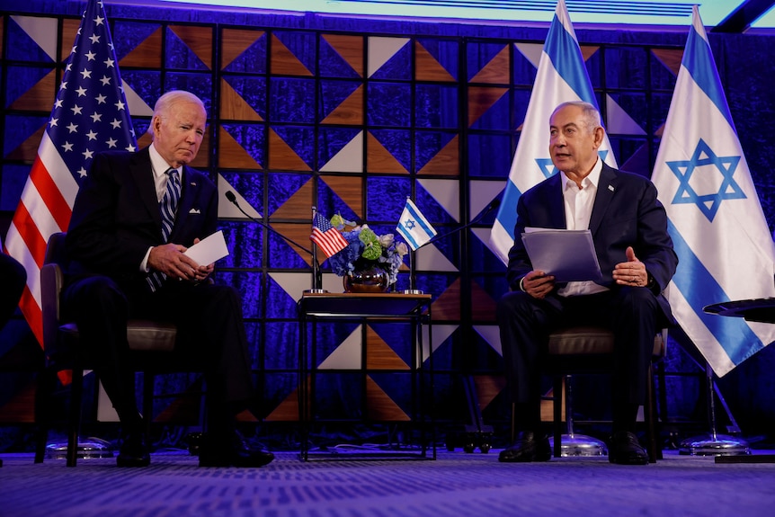 US President Joe Biden sits next to Israeli Prime Minister Benjamin Netanyahu on stage in front of their countrys' flags. 