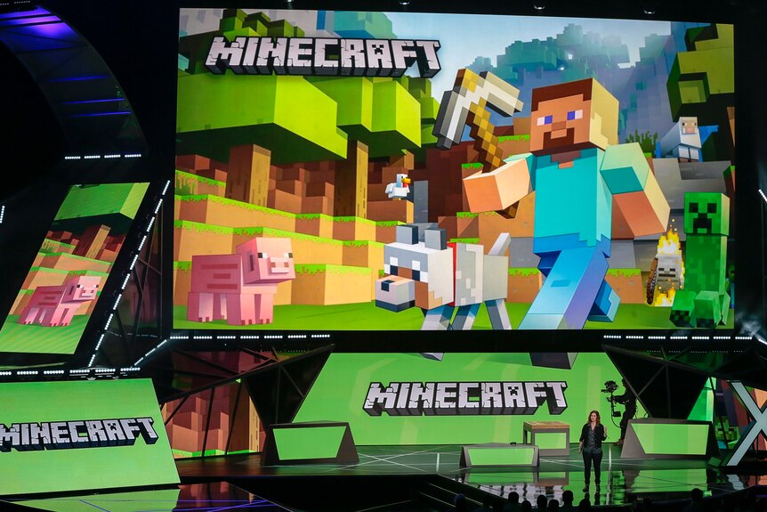 Lydia Winters stands on stage with signs showing Microsoft's Minecraft game at the Xbox E3 2015 briefing
