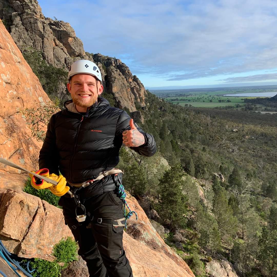 A man standing on a hillside wearing climbing gear and a helmet