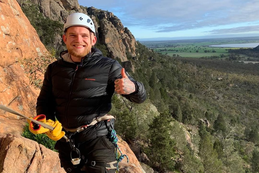 A man standing on a hillside wearing climbing gear and a helmet