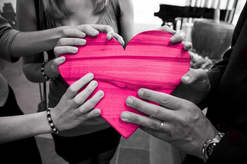 Monochrome hands holding a wooden heart with bright pink colouring