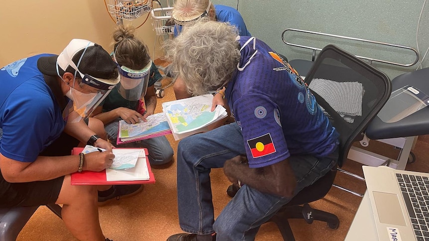 A group of people with face shields including an aboriginal man study a map.