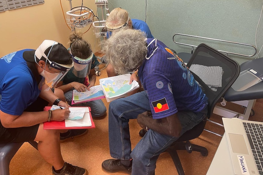 A group of people with face shields including an aboriginal man study a map.
