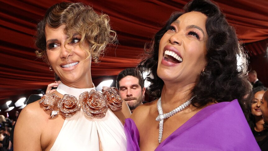 Angela Bassett in purple and Halle Berry in white with pink roses - both in formal gowns, Angela laughing