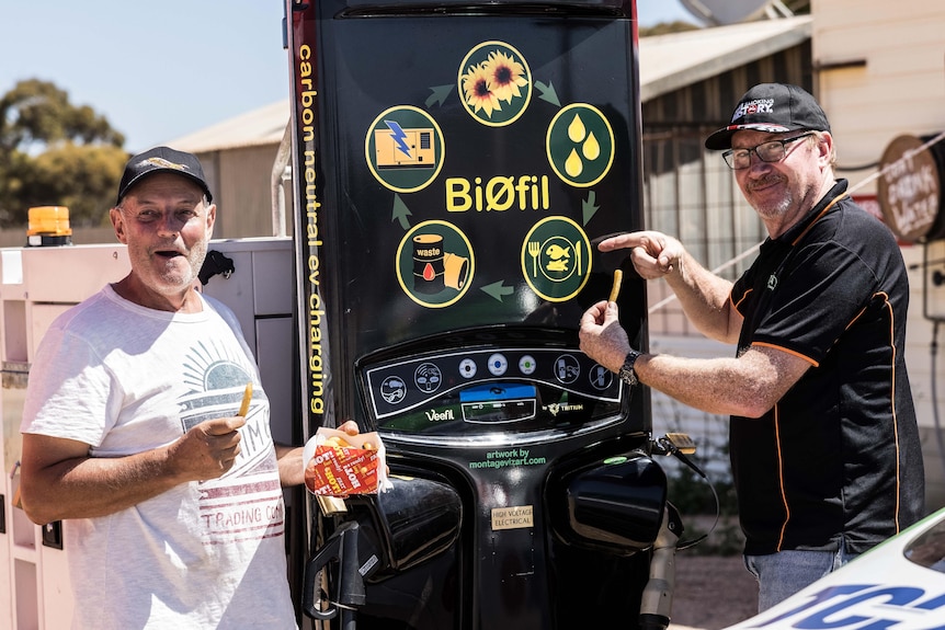 Two men holding chips in front of a electric vehicle charger. 