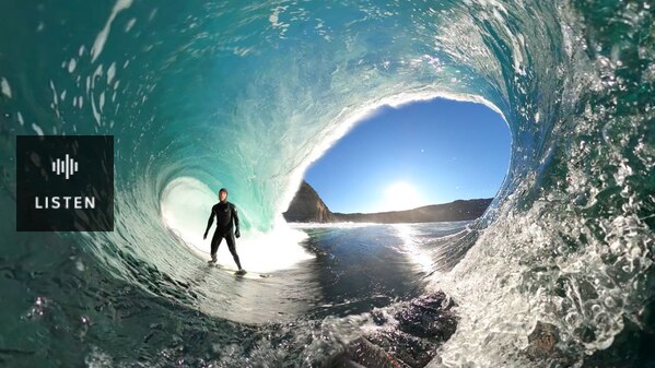 A man in a wetsuit surfs inside a giant, curling wave. Has Audio.