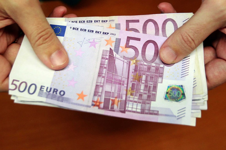 A close-up of a bank employee holding a pile of 500 euro notes.
