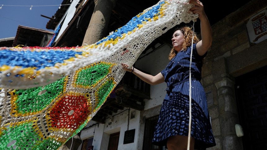 A woman is waving a weaved canopy made of recycled materials.