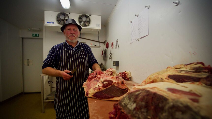 A butcher poses with a knife and a large hunk of meat.