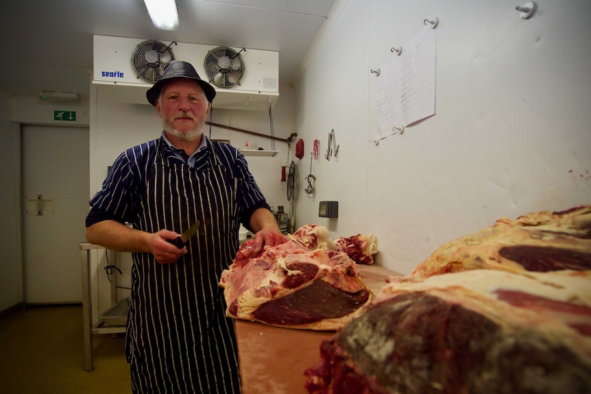 A butcher poses with a knife and a large hunk of meat.