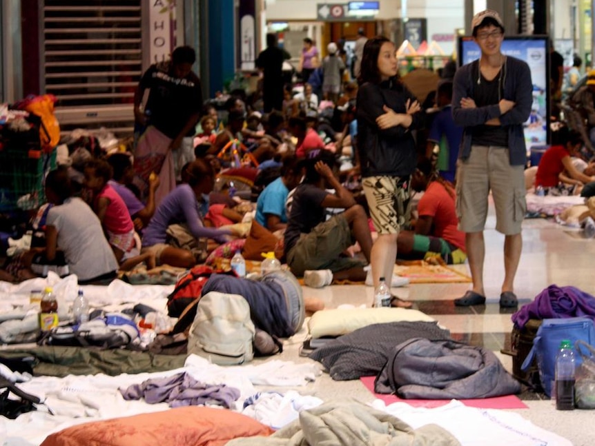 People with clothes, sleeping bags and pillows shelter in a shopping centre during a cyclone