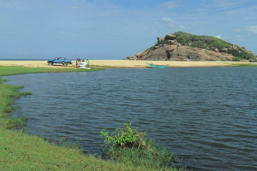 Sri Lankan police stand on a beach in the foreground of a large rock.