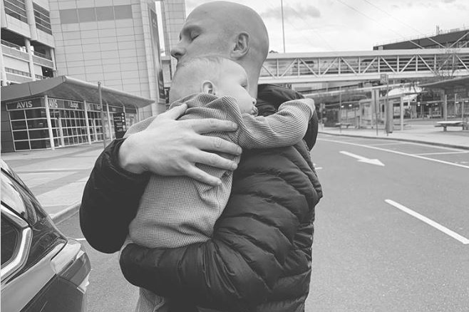 A black and white photo of Gary Ablett, with his eyes closed, holding his baby.