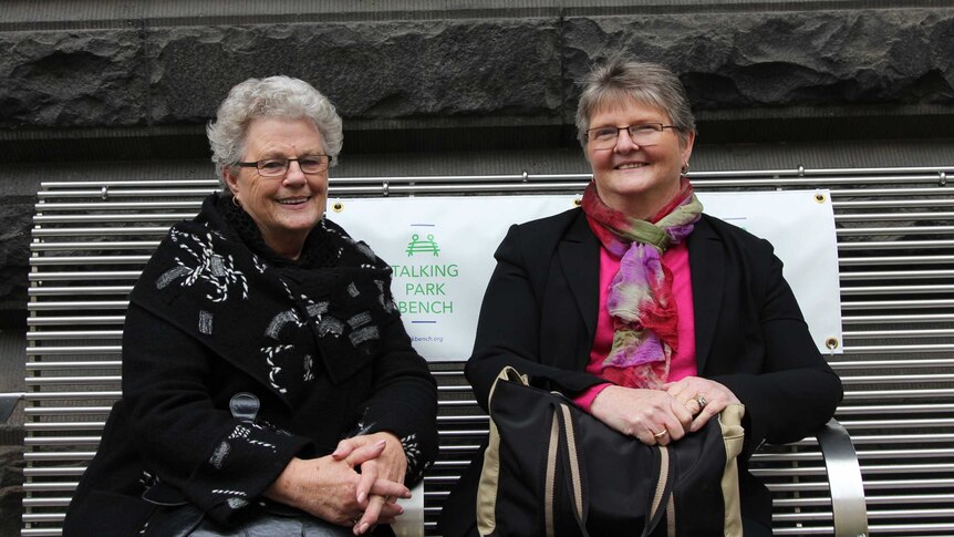 Sybil and Mary sit on a metal park bench outside Melbourne Town Hall.