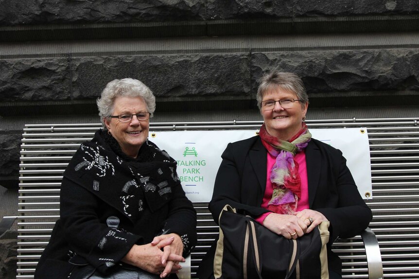 Sybil and Mary sit on a metal park bench outside Melbourne Town Hall.