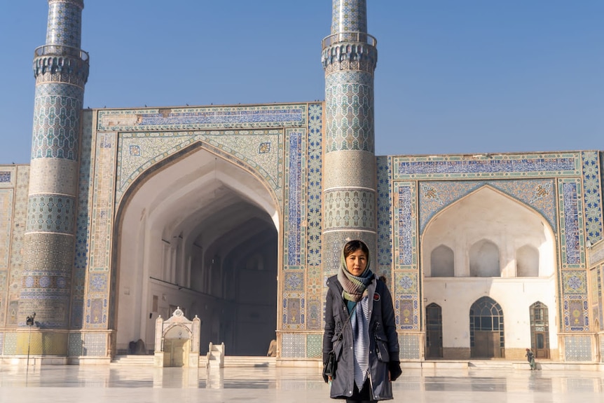 A woman stands in front of a mosque.