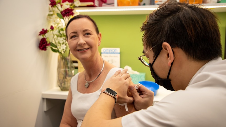 Yvette D'Ath in a white singlet smiling as she gets a needle.