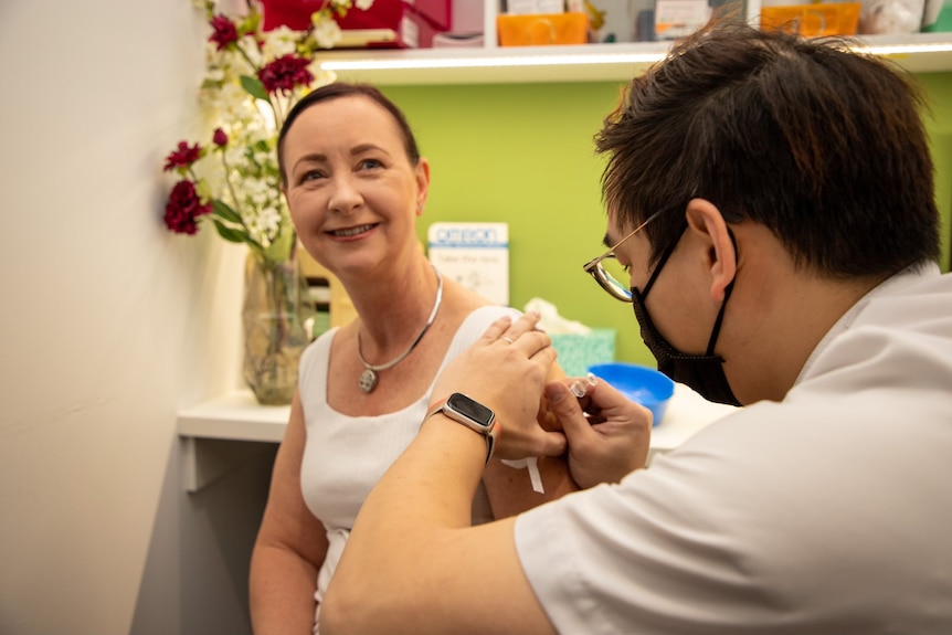 Yvette D'Ath in a white singlet smiling as she gets a needle.