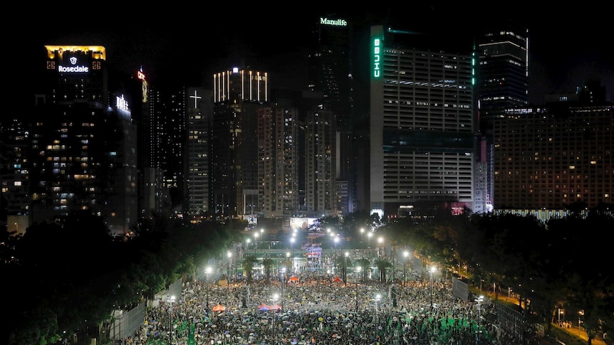 A main road in Hong Kong is blocked by a sea of demonstrators marching towards the skyline at night.
