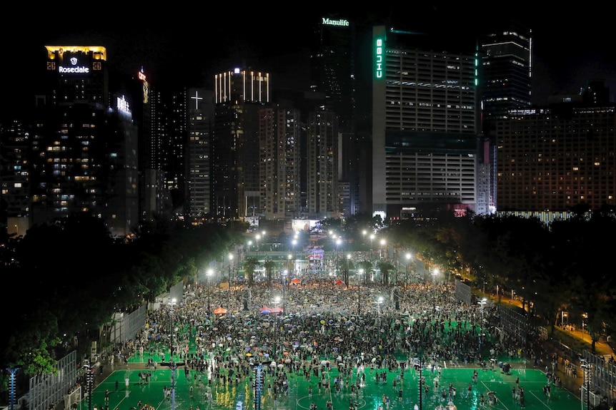 A main road in Hong Kong is blocked by a sea of demonstrators marching towards the skyline at night.