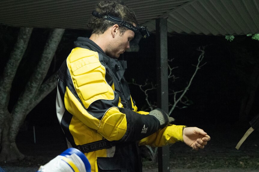 A man in a heavy, yellow motorbike jacket, headlamp and thick gloves adjusts his sleeve