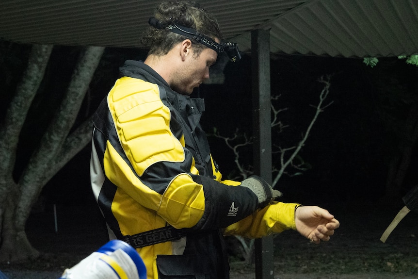 A man in a heavy, yellow motorbike jacket, headlamp and thick gloves adjusts his sleeve