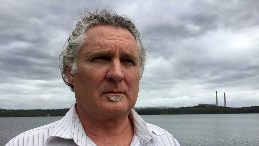 A headshot of a man looking out with Lake Macquarie in the background