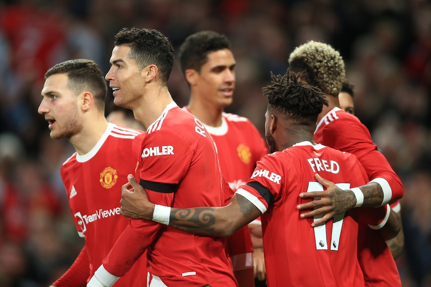 A group of Manchester United male players embrace as they celebrate a Premier League goal.