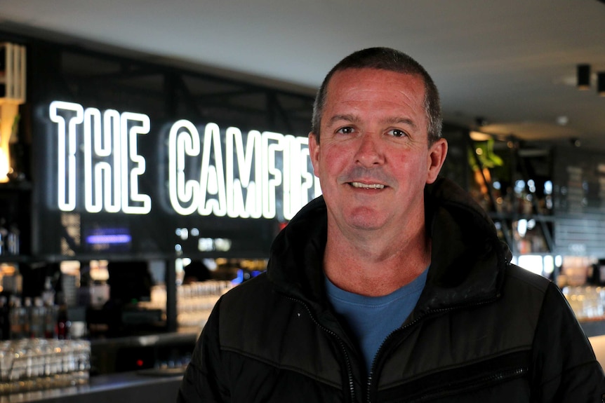 Mr McLernon stands in front of a neon sign saying "The Camfie..".