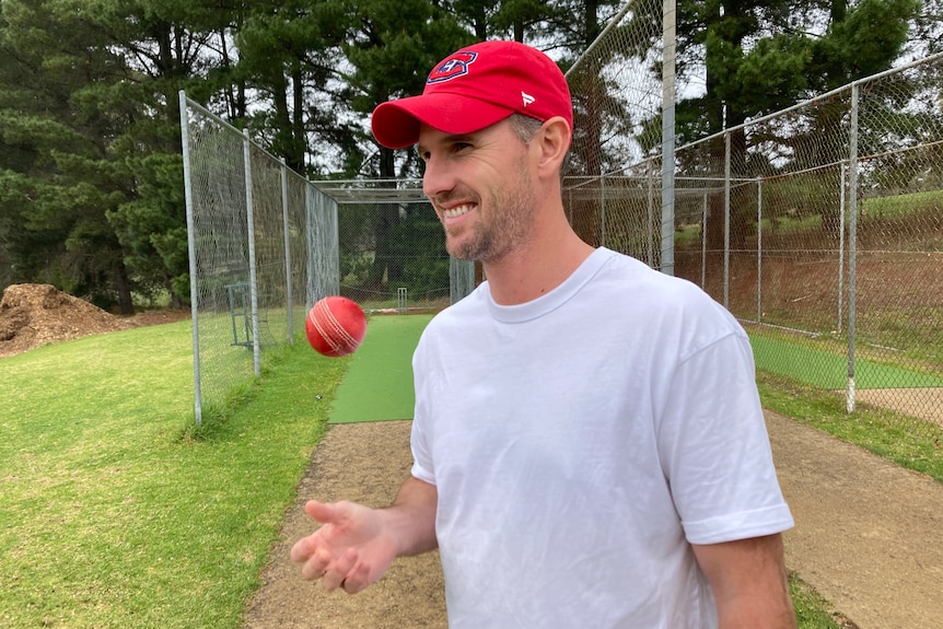 Shaun Tait throws a ball in the air in front of cricket nets.