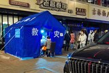 Masked people line up on a street outside a bright blue tent, where COVID tests are being administered