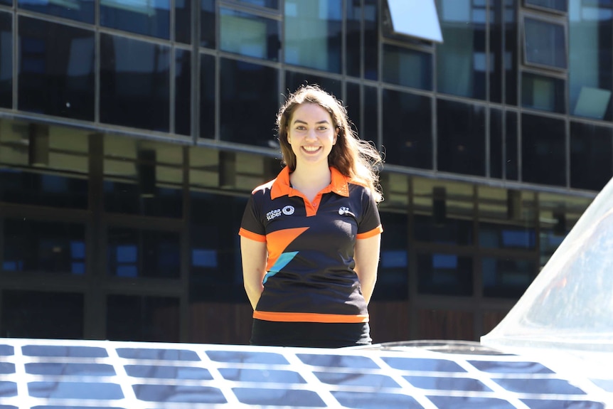 A woman stands behind a solar car.