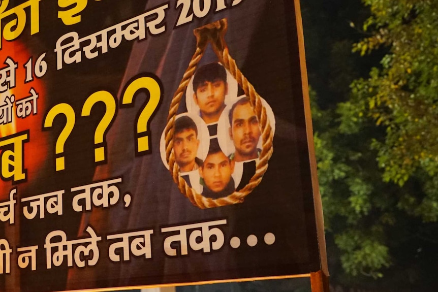 A billboard written in Hindi with the faces of four men pictured inside a noose