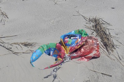 Deflated helium balloon on sand on a beach.