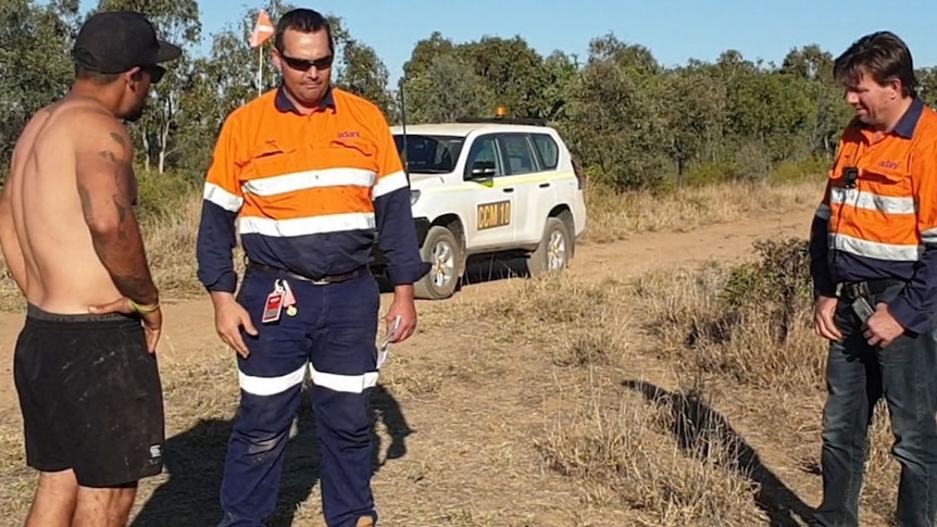 Two mine workers speaking with an Indigenous man on an undeveloped mine site