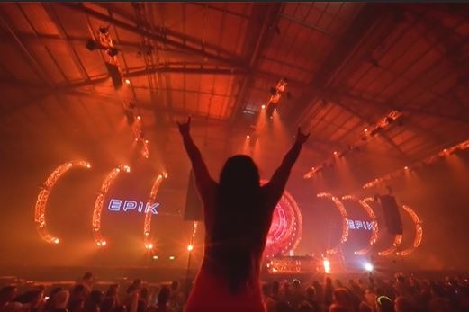 a silhouette of a woman with her hands in the air at a music festival 