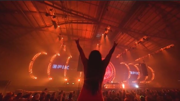 a silhouette of a woman with her hands in the air at a music festival 