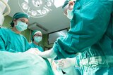 A surgeon and nurses stand over a patient in an operating theatre.