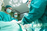 A surgeon and nurses stand over a patient in an operating theatre.