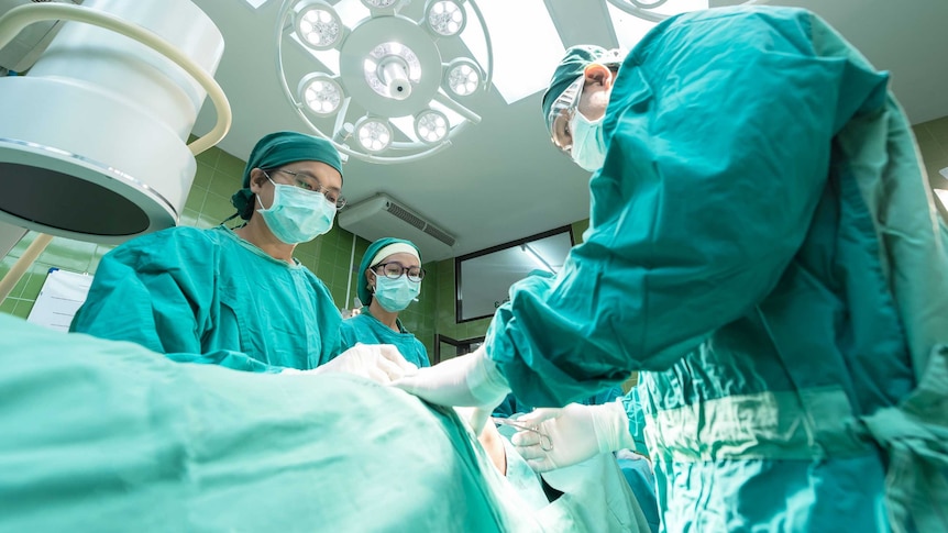A surgeon and nurses stand over a patient in an operating theatre.