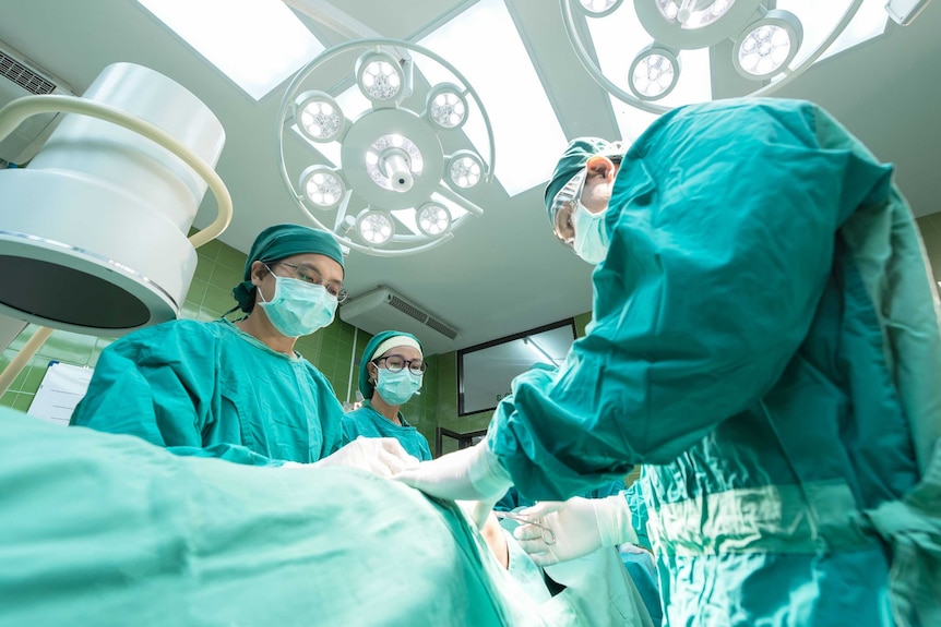 A surgeon and nurses stand over a patient in an operating theatre.