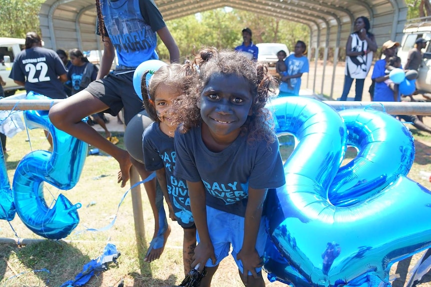 Two young Daly River fans in blue team tops smile at the camera.