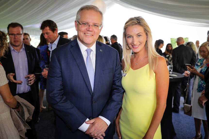 A woman in a yellow dress stands next to the prime minister in a blue suit for a photo.