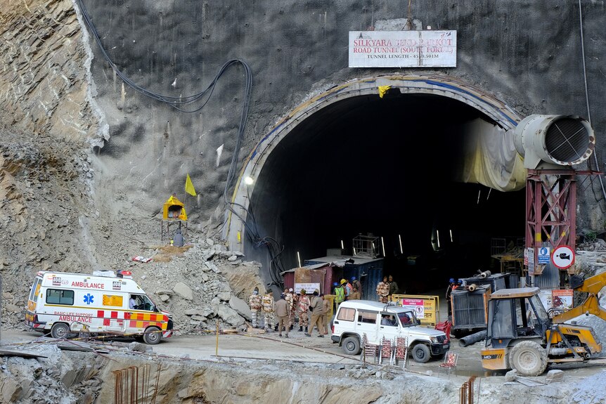 An ambulance sits near earthmoving equipment at the entrance to a large tunnel that is under construction.
