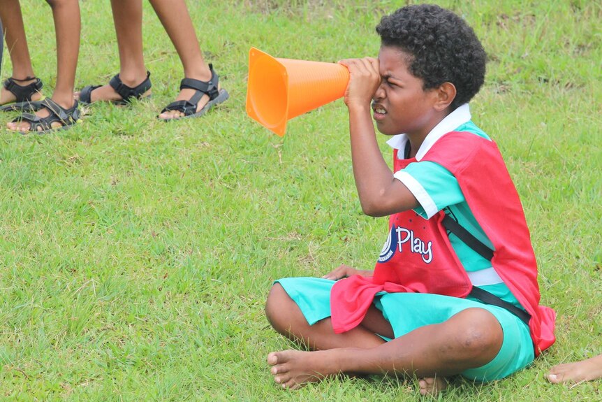 A girl sits down and uses a traffic cone as a telescope during a football clinic