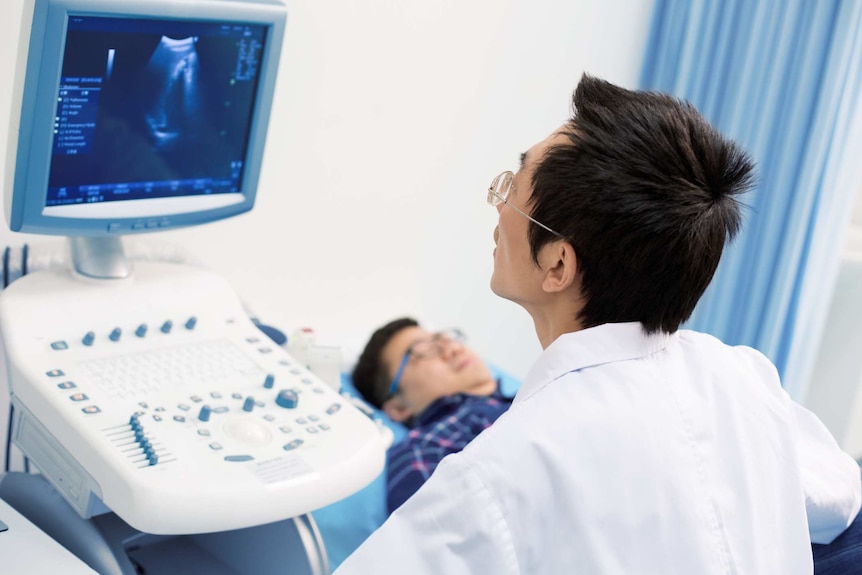 A man lies on a table while another person conducts an ultrasound